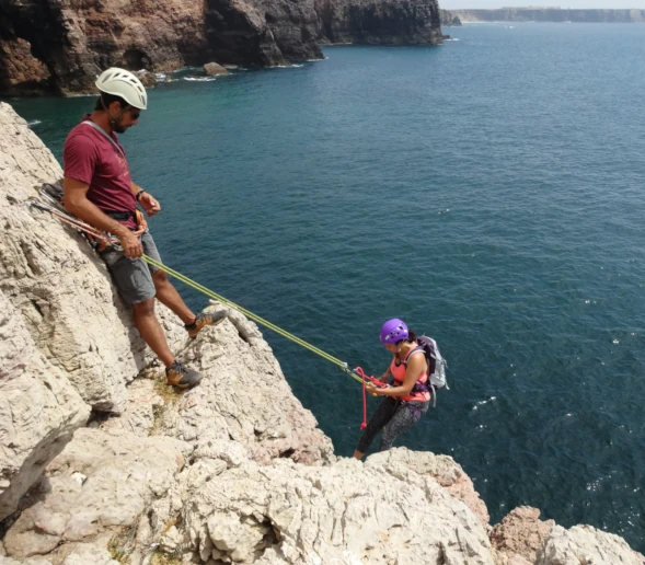 Climber supervising another abseiling down to the ocean.